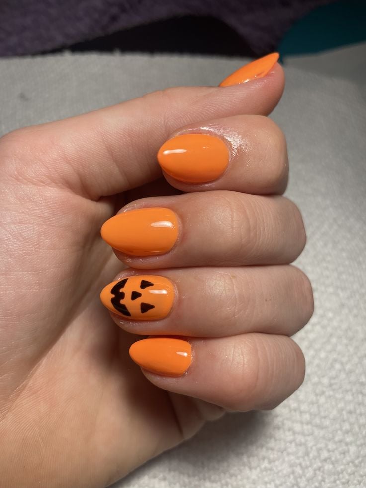 Almond shaped glossy nude and orange pumpkin nails for cozy fall season wear.