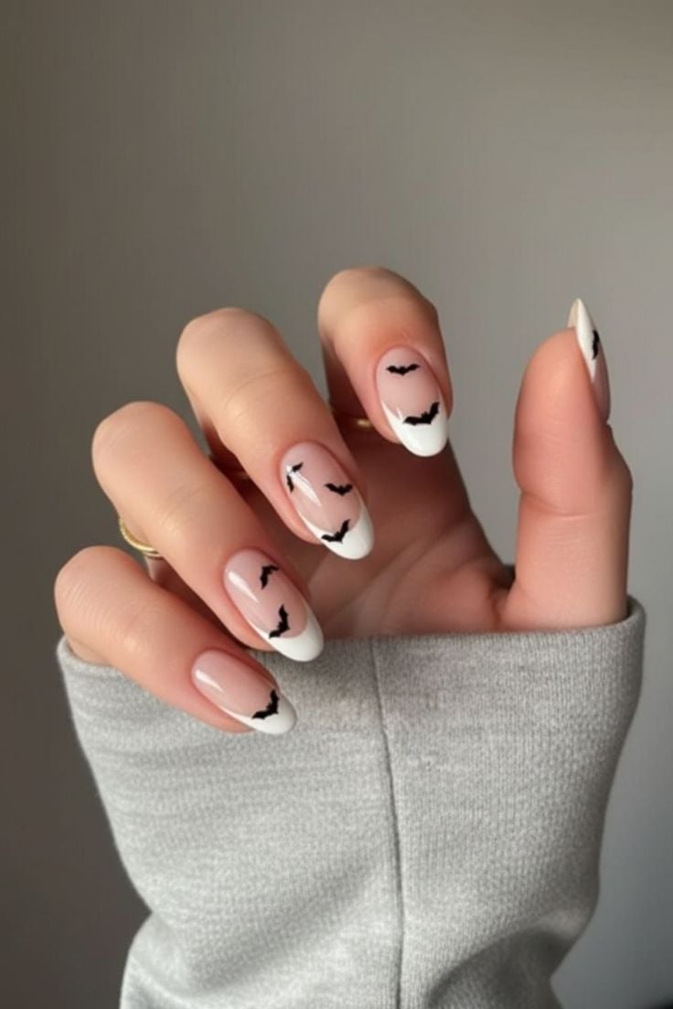 Short round glossy nude nails with tiny black bat and star illustrations.