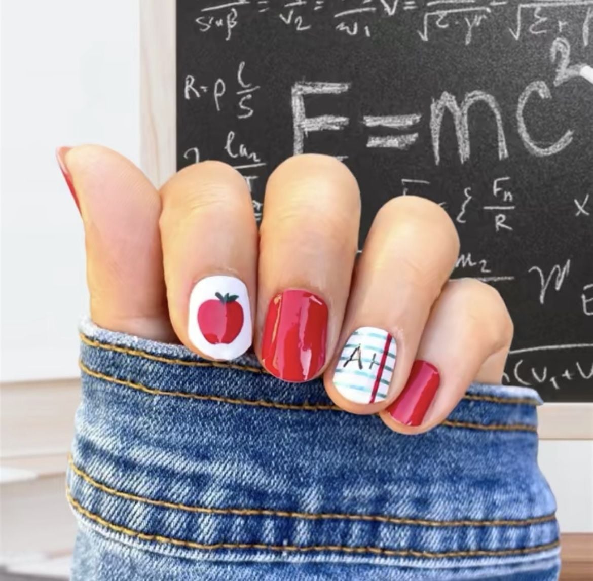 Short almond nails with deep red gel polish, metallic gold leaf accents, and red apple graphic.